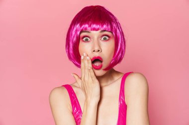 Şok olmuş peruklu güzel bir kadının görüntüsü pembe arka planda izole edilmiş kameraya şaşırdığını ifade ediyor.