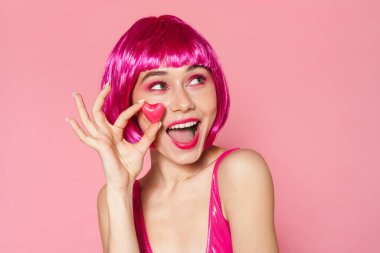 Pembe arka planda izole edilmiş şekerlerle poz veren peruklu güzel bir kadının görüntüsü