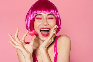 Pembe arka planda izole edilmiş şekerlerle poz veren peruklu güzel bir kadının görüntüsü