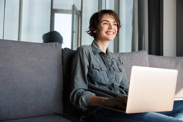 Imagem Agradável Jovem Mulher Satisfeita Usando Laptop Sorrindo Enquanto Sentado — Fotografia de Stock