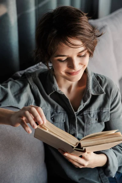 Esmer Hoş Memnun Kitap Okuyan Oturma Odasında Kanepede Otururken Gülümseyen — Stok fotoğraf