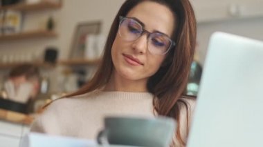 Gözlüklü çekici bir kadın, rahat bir kafede çalışırken kağıt belgeler izliyor.