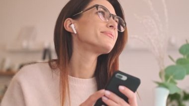 Kulaklıklı çekici bir kadının yakın çekim görüntüsü rahat kafede otururken akıllı telefonunu kullanıyor.