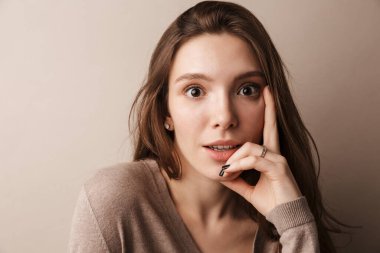 Gri duvardan izole edilmiş kameraya poz veren güzel bir kadının fotoğrafı.