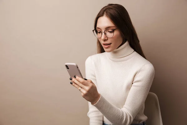 Foto Mulher Focada Encantadora Óculos Usando Celular Sentado Cadeira Isolada — Fotografia de Stock