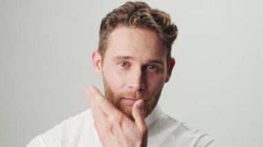 Beyaz gömlekli yakışıklı, neşeli, pozitif adam beyaz duvar arkasında izole edilmiş.