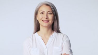 Uzun gri saçlı, resmi iş kıyafetleri giyen, mutlu, olgun bir kadın stüdyoda beyaz arka planda tek başına sırıtıyor.