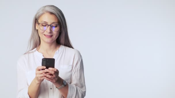 Uśmiechnięta Dojrzała Kobieta Długimi Siwymi Włosami Okularach Trzyma Swój Smartfon — Wideo stockowe