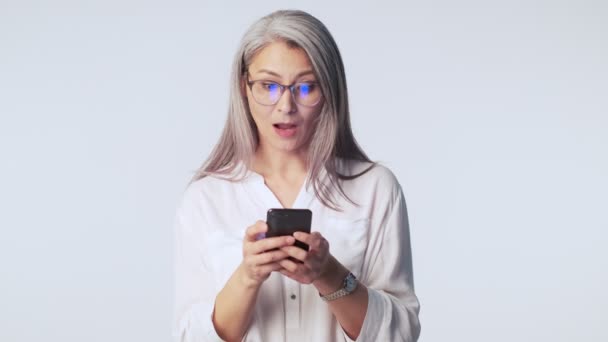 Zdziwiona Dojrzała Kobieta Długimi Siwymi Włosami Okularach Używa Swojego Smartfona — Wideo stockowe