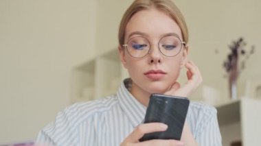 Gözlük takan genç ve güzel bir mimar ofiste otururken akıllı telefonunu kullanıyor.