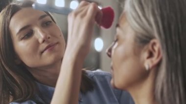 Çekici bir makyöz, güzellik salonunda makyaj fırçası olan yaşlı ve hoş bir kadına makyaj yapıyor.