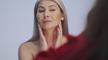 Güzel, yarı çıplak bir kadın stüdyodaki gri arka plandan izole edilmiş fotoğrafçıya poz veriyor.