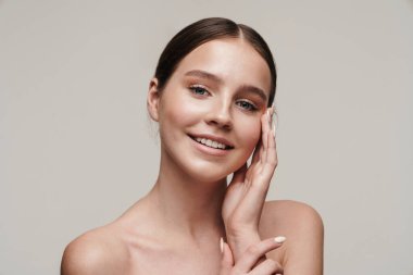 Neşeli, üstsüz, gülümseyen ve gri arka planda izole edilmiş kameraya bakan bir kadın resmi.