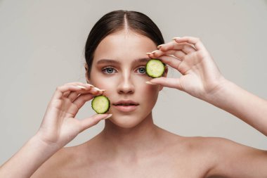 Gri arka planda izole edilmiş kamerada salatalıkla poz veren güzel üstsüz bir kadın resmi