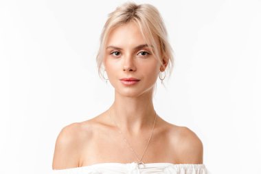 Küpeli güzel sarışın bir kadın resmi. Beyaz arka planda izole edilmiş kameraya bakıyor ve poz veriyor.