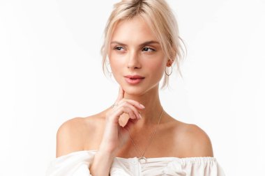 Küpeli sarışın bir kadının beyaz arka planda izole bir şekilde poz verirken ve bakarken görüntüsü.