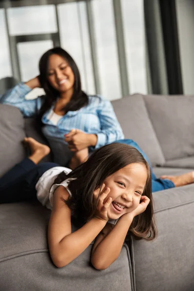 照片中快乐的亚洲孕妇和她的小女儿在沙发上休息的时候笑了 — 图库照片
