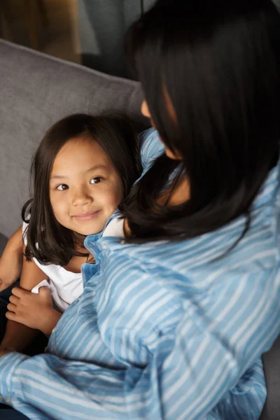 年轻的亚洲孕妇和她的小女儿坐在沙发上拥抱的照片 — 图库照片