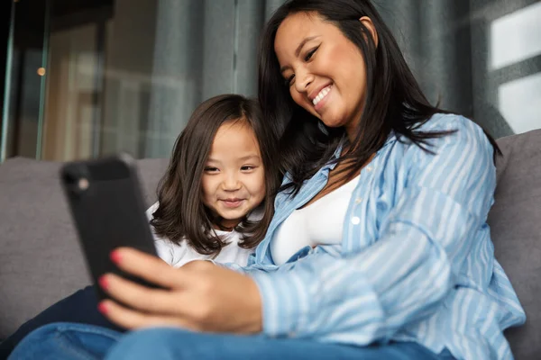 Evdeki Kanepede Otururken Küçük Kızıyla Gülümseyen Cep Telefonu Kullanan Neşeli — Stok fotoğraf