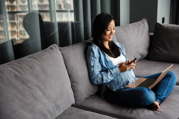 Foto Einer Lächelnden Schwangeren Asiatin Die Laptop Und Handy Benutzt — Stockfoto