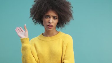 Sıkıcı, kıvırcık saçlı, genç, Afro-Amerikan bir kadın elini mavi duvar arkasında, stüdyoda yalnız bir şekilde işaret ediyor. Anlamsız, sıkılmış, iğrenç içerik