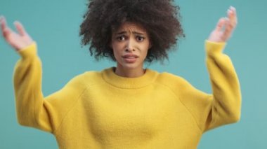 Şaşırmış, duygusal, kıvırcık saçlı Afro-Amerikan bir kadın elini kaldırıyor. Stüdyonun mavi duvarından izole edilmiş arka planına.