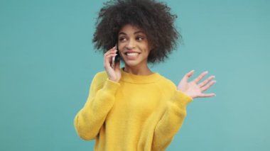 Kıvırcık saçlı, gülümseyen Afro-Amerikan bir kadın telefonda konuşuyor.