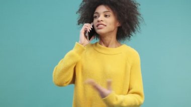 Kıvırcık saçlı, duygusal bir Afro-Amerikalı kadın telefonda konuşurken ellerini stüdyonun mavi duvarından soyutlamış bir şekilde işaret ediyor.
