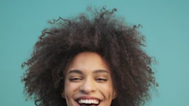 Mutlu, duygusal, Afro-Amerikan bir kadının yakından çekilmiş görüntüsü stüdyoda mavi duvarın arkasında tek başına gülüyor.