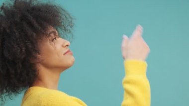 Mutlu ve genç bir Afrikalı Amerikalı kadının yan görüntüsü stüdyodaki mavi duvarın arkasında dans ediyor.