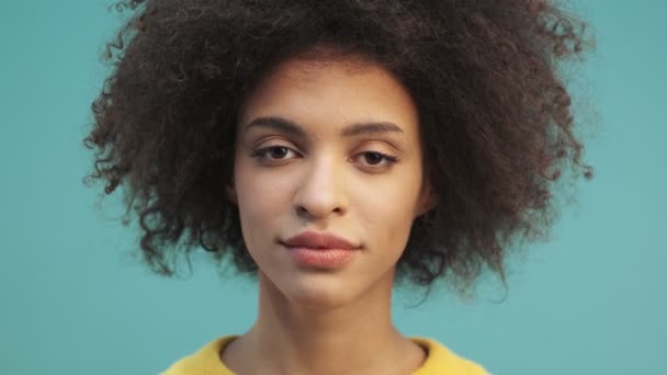 一个有着一头卷发的快乐的年轻的非洲裔美国女人的特写镜头让她开开开眼界 笑着看着独立站在蓝墙背景下的摄像机 — 图库视频影像