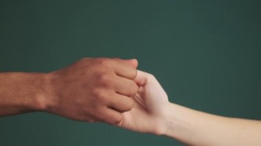 Genç çokuluslu ellerin yakın plan görüntüsü büyük parmaklarla oyun oynuyor ve stüdyodaki yeşil duvar arka planında izole edilmiş şekilde eğleniyorlar.