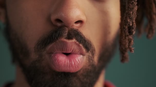 若いアフリカ系アメリカ人の男の唇の閉じ込められたクリップは エアキスを送信しているか スタジオで緑の壁の背景に隔離された吹いています — ストック動画