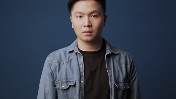一个穿着休闲装的自信而严肃的亚洲年轻人站在工作室深蓝色墙壁的背景上 表现出一种 的姿态 — 图库视频影像