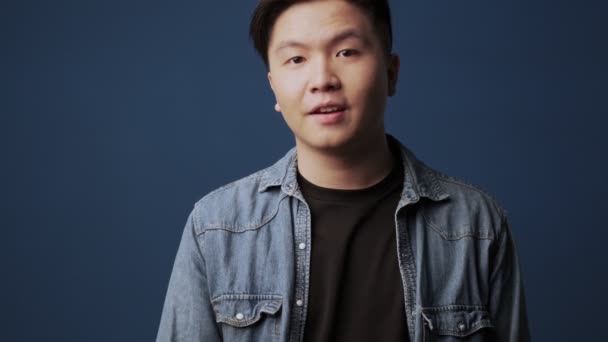 一名身穿休闲装 面带微笑的亚洲年轻人在工作室的深蓝色墙壁背景上做着一个很好的手势 — 图库视频影像