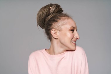 Gri arka planda izole bir şekilde duran ve bakışlarını başka yöne çeviren, Rastalı saçları olan çekici bir genç kadının portresi.