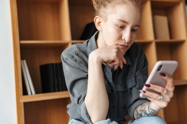 Rasta takmış, rafların yanında piercing takmış, cep telefonuyla sohbet eden güzel bir kızın resmi..