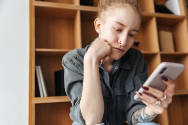 Rasta takmış, rafların yanında piercing takmış, cep telefonuyla sohbet eden güzel bir kızın resmi..