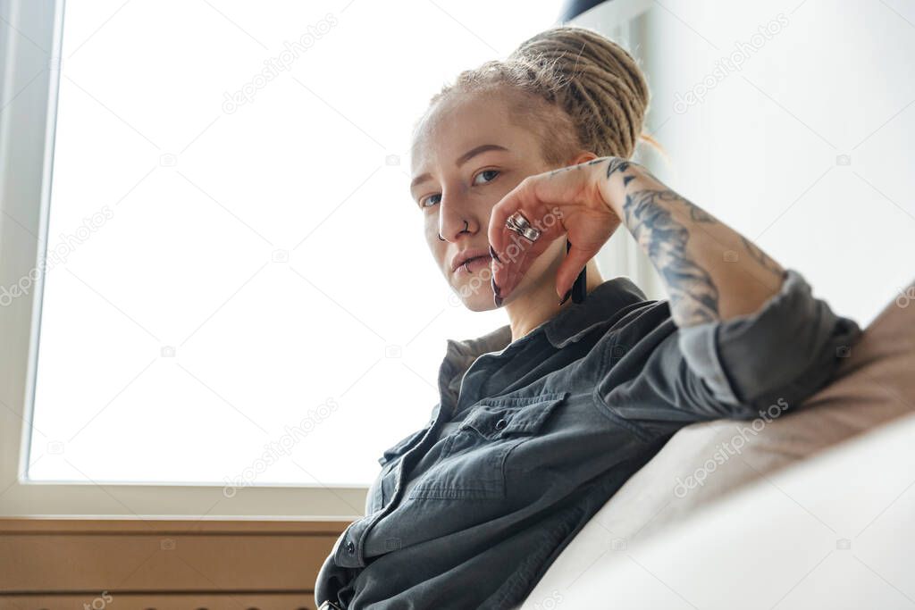 Image of a serious young girl with dreadlocks and piercing indoors near window.