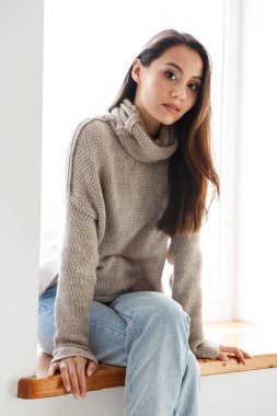 Pencere pervazında otururken kameraya bakan güzel Asyalı kadın görüntüsü