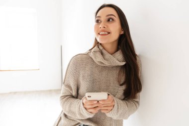 Duvara yaslanırken gülümseyen ve akıllı telefon kullanan neşeli Asyalı kadın görüntüsü