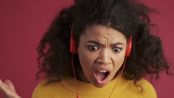 年轻的非洲姑娘尖叫着负压的女人被深红色的勃艮第背景隔离 用耳机听着音乐 — 图库视频影像