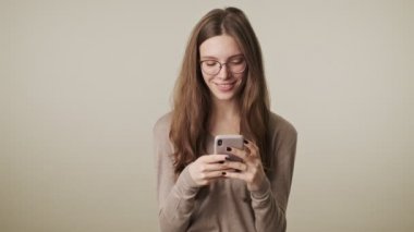 Güzel, genç, mutlu, güzel bir kadın. Gri duvar arka planında izole edilmiş. Cep telefonu kullanıyor.