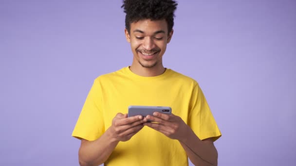 若いですアフリカの幸せな男分離上の紫の背景見る面白いビデオによって携帯電話 — ストック動画