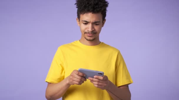 若いアフリカの感情的な男隔離された以上の紫の背景ゲームによって携帯電話 — ストック動画