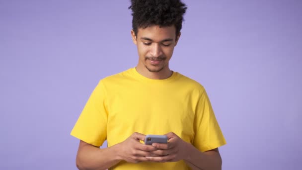 若いアフリカの濃縮男は 携帯電話を使用して紫の背景に隔離された — ストック動画