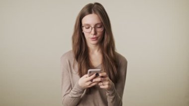 Sana el sallayan cep telefonuyla gri duvar arkaplanından izole edilmiş genç, konsantre tatlı bir kadın.