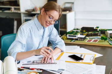 İş yerinde taslak tasarlarken pusula ile resim yapan gülümseyen kadın mimar.