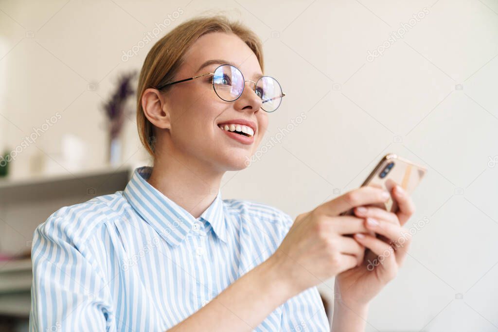 Photo happy nice woman architect in eyeglasses using mobile phone while designing draft at workplace