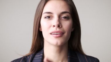 Güzel, gülümseyen bir kadının yakın plan görüntüsü stüdyodaki beyaz arka planda izole bir şekilde duran gizli bir jest yapıyor.